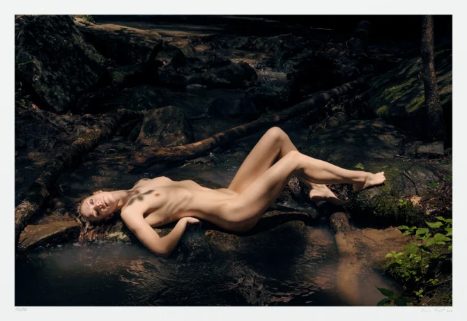 In this landscape art photograph, a nude woman bathes in a small stream