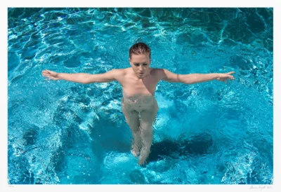 In this colorful art photograph, a nude woman stands in a swimming pool. She extends both arms symmetrically, forming a an unmistakable cross shape.