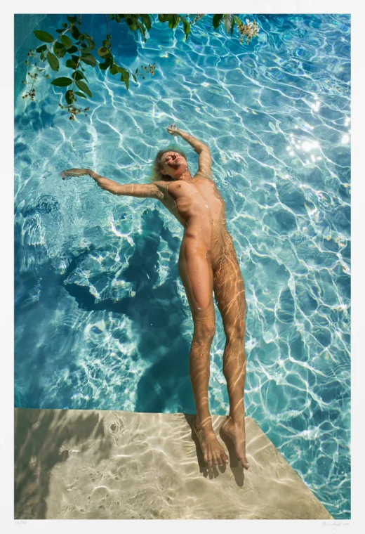 In this art photograph a nude woman drifts on her back in a gleaming blue swimming pool. Her only interest seemingly is this joyful moment of sun and water